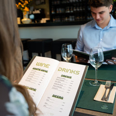 Two guests sitting in a restaurant looking at a personalised drinks menu cover