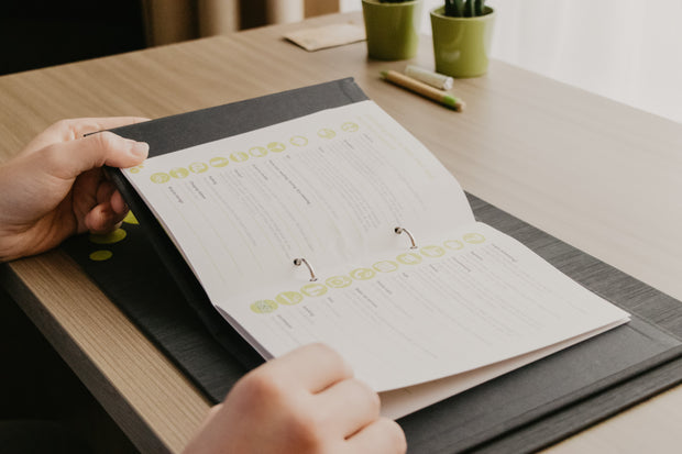 Person holding a planner with fishing-themed design on a wooden table.