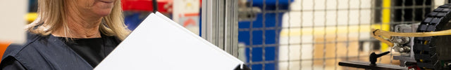 Person holding a hard cover in front of a machine in an industrial setting doing quality checking